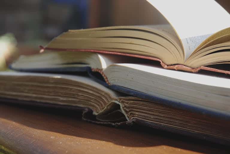 Closeup stack of opened books in hardcover placed on wooden table on sunny terrace