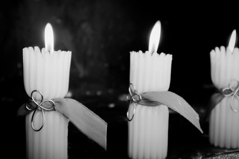 Black and white photo of three decorative candles with ribbons and flame.